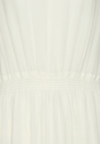 Valkoinen, kevyt kangasmekko, jossa on kootut vyötärö ja pehmeät laskokset, jotka luovat virtaavaa laskostusta. Sujuva pinta, minimalistinen muotoilu.