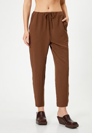Pantalons marron, légers, texturés avec une taille élastique, un cordon de serrage et des poches latérales ; associés à des sabots à talons épais marron foncé.