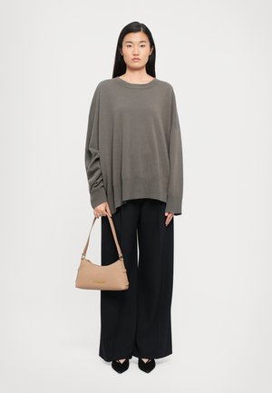 Maglione grigio oversize, pantaloni neri larghi e una borsa beige. La texture è liscia, la vestibilità è morbida e i tacchi neri a punta completano il look.