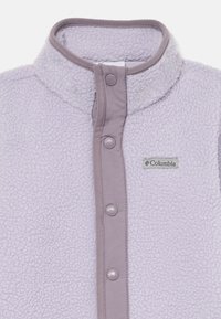 Světle fialová fleecová vesta s vysokým límcem, patentkami a logem Columbia na levé straně. Měkká textura a kontrastní lem.