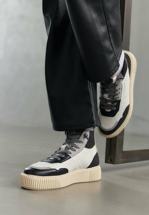 Sneakers alte con pelle nera e bianca, dettagli grigi testurizzati e una suola spessa color crema. Design con lacci e dettaglio del logo visibile.