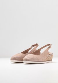 Beige sleehakken met een suède textuur, open achterkant en enkelbandje. Beschikbaar met een geweven jute accent langs de sleehak. Rond neuzen ontwerp.