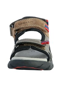 Sandalia marrón y gris con correas ajustables, suela de goma y acentos rojos y azules. Diseño abierto con material texturizado y detalles de costura.