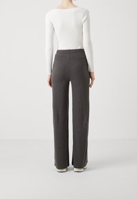 Szare, prążkowane spodnie z szerokimi nogawkami mają wysoki pas i miękką teksturę. Są zestawione z dopasowaną, białą bluzką z długim rękawem, pokazane od tyłu.