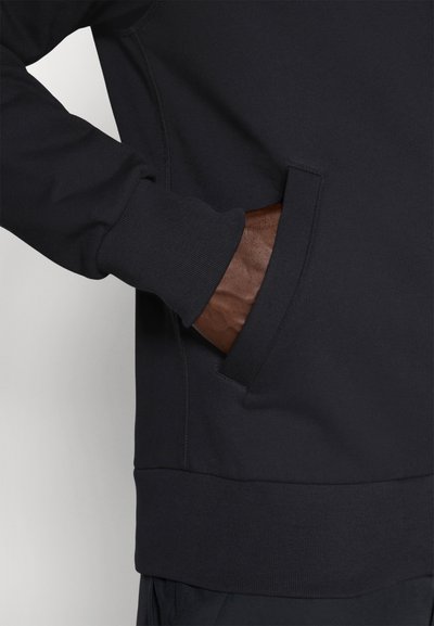 Sweatshirt noir avec une poche latérale, des poignets et une taille côtelés. Texture de tissu lisse avec des détails de couture visibles.