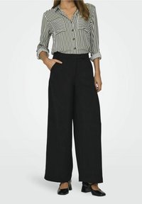 Pantalons larges noirs à taille haute, associés à une chemise à rayures à boutons avec des poches poitrine et des manches retroussées.