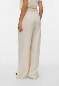 Szerokie spodnie z kremowej tkaniny, z elastycznym pasem i gładką fakturą. Brak widocznych wzorów ani elementów ozdobnych.
