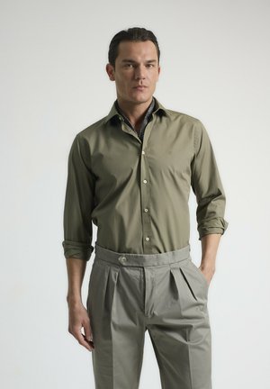 Camisa de botones verde oliva con mangas largas, combinada con pantalones grises de cintura alta con pliegues. Tejido suave, diseño de cuello clásico.
