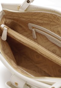Hvid lædertaske indvendigt med en glat tekstur, guldlynlås og flere rum. Forret med et beige stof med et logo-mønster.