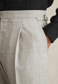Checked high-waisted trousers in light gray, featuring a textured fabric, pleats, and a side pocket with a belt loop detail.