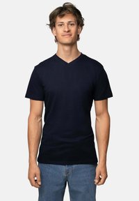 Námořnická modrá, krátký rukáv, tričko s v-výstřihem z měkké tkaniny; přiléhavý střih s hladkým povrchem; nošeno s světle modrými džíny.