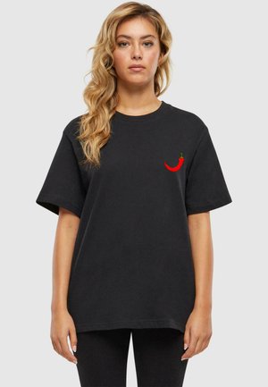 Schwarzes Baumwoll-T-Shirt mit kurzen Ärmeln, mit einer roten Chili-Pfeffer-Stickerei auf der linken Brustseite. Lässiger Schnitt mit Rundhalsausschnitt.