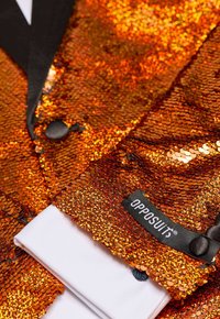 Blazer de lentejuelas naranjas brillantes con solapas negras, puños de camisa blanca en contraste y etiqueta "OPPOSUIT", que muestra colores vivos y una textura intricada.