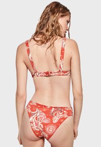 Conjunto de bikini rojo con un patrón de paisley, tirantes ajustables y cierre en la espalda. La tela tiene una textura suave con un diseño vibrante.
