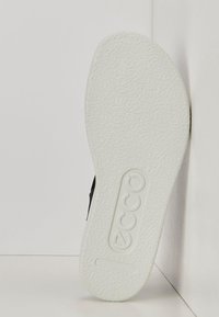 Musta kenkä, jossa on teksturoitu valkoinen kumipohja, jossa on Ecco-brändi ja "DANISH DESIGN" -painatus. Suora muoto korostaa sen minimalistista muotoilua.