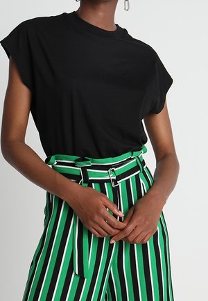Person wearing a black short-sleeve top paired with high-waisted green, white, and black vertically striped pants with a matching belt.