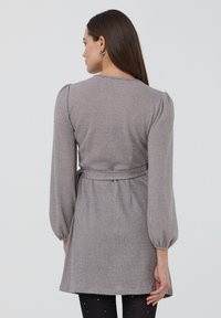 Vestito in maglia grigio con maniche lunghe a sbuffo, vita con cintura e finitura testurizzata. L'orlo cade sopra il ginocchio, creando una silhouette aderente.
