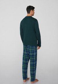 Męski zestaw do noszenia w domu składający się z ciemnozielonej bluzki z długim rękawem oraz niebieskich spodni w kratę z białymi i zielonymi liniami, wykonany z miękkiego materiału.