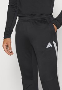 Schwarze Sporthosen aus strukturiertem Stoff, mit einem weißen diagonalen Akzent und dem Adidas-Logo auf der linken Seite. Sichtbarer elastischer Bund.