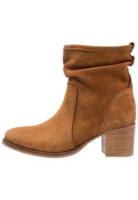 Bruna mockaskinnsankelkängor med en slouchy design, rund tå och en staplad träklack. Har dekorativ sömnad längs sömmen.