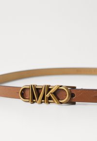 Leren riem in tan kleur met een gouden metalen logo-gesp met de letters "CMK." De gladde textuur en het dunne ontwerp benadrukken eenvoud.