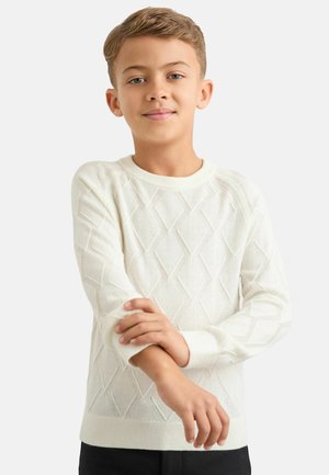 Biały sweter dziergany z wzorem w romby, zaokrąglonym dekoltem i ściągaczami przy mankietach. Model krzyżuje ramiona, ma na sobie czarne spodnie.