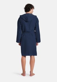 Accappatoio blu navy con cappuccio, maniche lunghe e vita legata, realizzato in tessuto morbido e liscio, con taglio alla lunghezza del ginocchio.