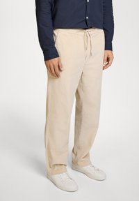 Pantalones de pana beige con cintura ajustable, con acanalado vertical y un corte relajado, combinados con zapatillas blancas.