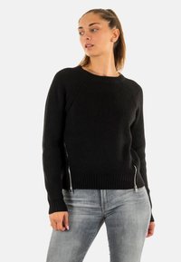 Suéter negro de canalé con mangas largas, cuello redondo y detalles de cremallera plateada a los lados. Fabricado en un tejido de punto texturizado.