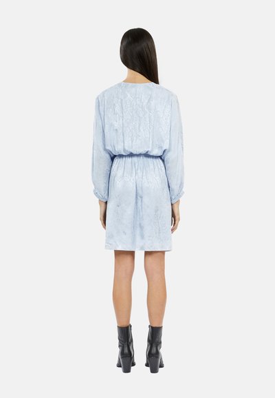 Un vestido azul claro, texturizado, con cintura ceñida y mangas largas, con un dobladillo hasta la rodilla y un acabado liso y brillante. Botines negros.