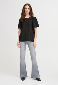 Top nero strutturato con maniche a sbuffo, abbinato a jeans grigi chiari a palazzo e scarpe nere a punta. Design minimalista, outfit casual.