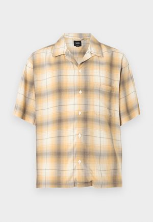 Chemise à manches courtes à boutons avec motif à carreaux jaune, beige et marron, une poche poitrine, posée à plat sur fond blanc.