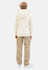Sweat-shirt crème avec capuche à cordon, associé à un pantalon cargo beige avec poches latérales, sur fond blanc uni.