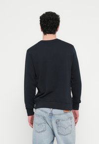 Tengerészkék pulóver bordázott mandzsettákkal és derékrésszel, kerek nyakkivágással. Az anyag puha és texturált hatású. Világoskék farmerral viselve.