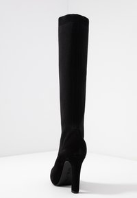 Botte noire ajustée à hauteur de genou avec un talon en daim doux et un tige en tissu élastique, présentant un haut en tricot côtelé pour un supplément de texture.