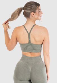 Olivgrön sportbh med korskorsade axelband och en texturerad tyg. Parat med högmidjade matchande leggings med accentuerande sömmar.