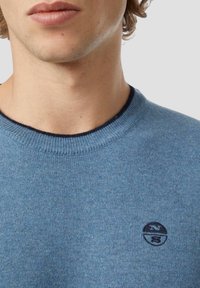 Maglione lavorato a maglia blu con scollo rotondo e bordo blu navy. Presenta un piccolo logo ricamato sull'area del petto sinistro. Texture morbida.