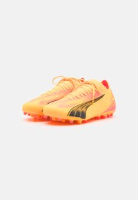 Botas de fútbol amarillas con acentos negros, parte superior texturizada y un ajuste ceñido; cuenta con tachones de goma rosa para tracción en superficies de hierba.