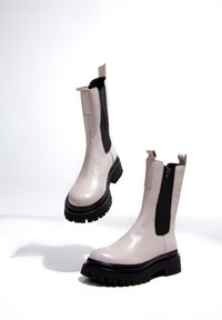 Botines beige claro con acabado de cuero liso, paneles laterales elásticos negros, suela gruesa de goma negra y tira trasera para facilitar su colocación.