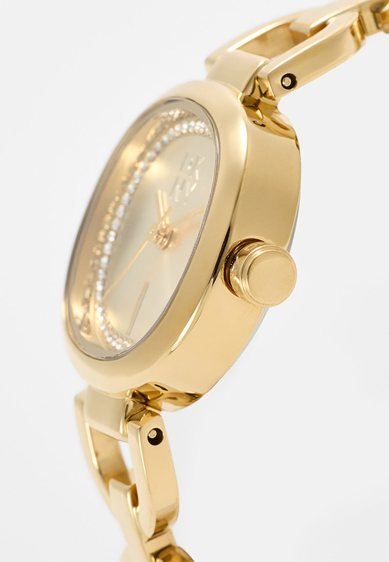 Reloj en tono dorado con una caja redonda, correa metálica, acentos de cristal en el bisel y una esfera dorada clara con marcadores de horas minimalistas.