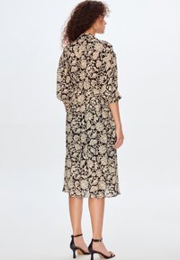Vestito floreale nero e beige con vestibilità ampia, maniche a tre quarti e lunghezza al ginocchio, realizzato in tessuto leggero. Sandali neri con tacco.
