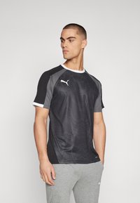 Fekete sportpóló, textúrált, hullámos mintával, rövid ujjú, fehér részletekkel és Puma logóval a mellkason. Sportolásra alkalmas.