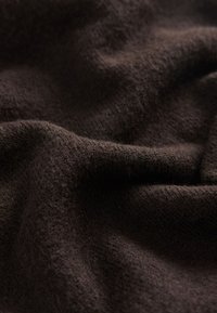 Tissu doux marron foncé avec une texture tissée visible et des plis légers créant des ombres et des reflets.