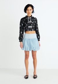 Fekete virágmintás, rövid farmer blúz puffos ujjal, ezüst hardware-rel, világoskék, bővülő szoknyával párosítva. A szettet fekete lapos cipők egészítik ki.