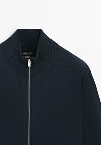 Pull en coton côtelé bleu marine avec col montant et fermeture éclair argentée à l'avant, étiquette Massimo Dutti.