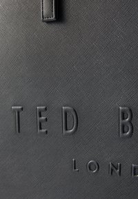Bolso tote negro con textura que presenta la lettering en relieve "TED BAKER LONDON", con un acabado suave y un diseño estructurado.
