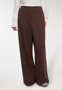 Brązowe spodnie z szerokimi nogawkami, wykonane z gładkiego materiału, z zapięciem na guziki z przodu, bocznymi kieszeniami oraz luźnym, swobodnym krojem.