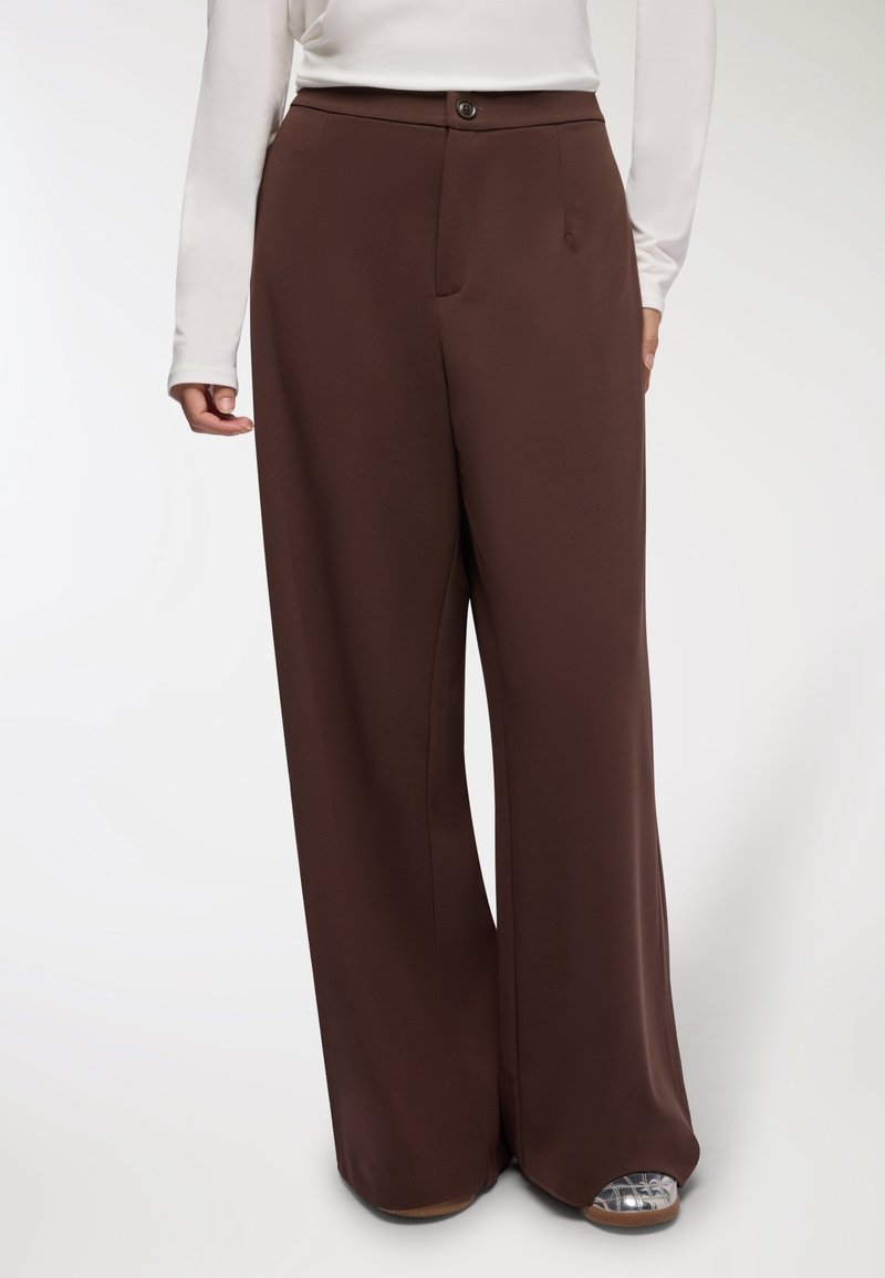 Brązowe spodnie z szerokimi nogawkami, wykonane z gładkiego materiału, z zapięciem na guziki z przodu, bocznymi kieszeniami oraz luźnym, swobodnym krojem.