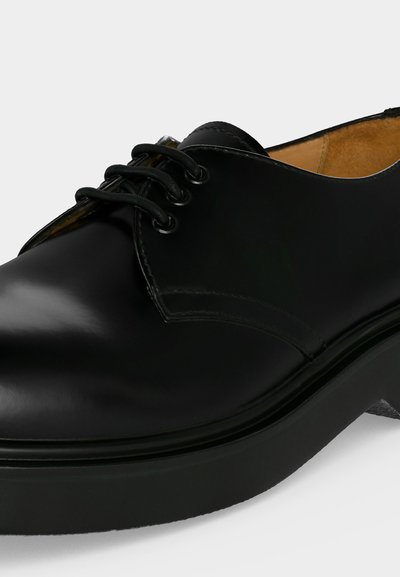 Chaussure formelle en cuir noir avec bout arrondi, trois œillets avec lacets noirs, semelle épaisse et doublure intérieure beige.