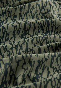 Textil i olivgrönt med ett texturerat svart abstrakt mönster. Har en slät finish och en något skrynklig yta.